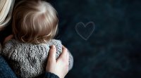Young blonde girl in knit sweater draws heart shape on foggy window, creating atmospheric moment of childhood wonder and contemplation on dark winter day.