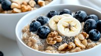 Healthy breakfast bowl with oatmeal, fresh blueberries, sliced banana, walnuts and chia seeds on white background. Close up view of nutritious morning meal.