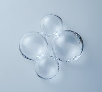 Clear glass spheres arranged in clover pattern on light background, creating minimalist composition with reflective surfaces and subtle shadows.