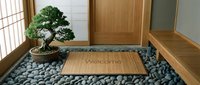 Zen Japanese entryway with welcome mat, bonsai tree, river stones, and wooden door creating a calm, minimalist home entrance.