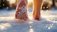 Bare feet walking in fresh snow at sunset with magical golden bokeh lights, creating dreamy winter atmosphere. Close up view captures frosty sensation and natural warmth.