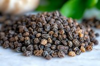 Dried black peppercorns in green leaf background, macro view showing texture and natural spice details.