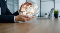 Businessman in dark suit holding glowing geometric crystal structure on wooden desk in modern office environment, representing innovation, technology, and business solutions.