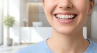Young woman with metal braces smiling showing orthodontic treatment in modern dental office. Teeth straightening and oral health care concept.