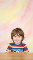 Young boy with light brown wavy hair and fair complexion wearing colorful striped shirt, smiling at camera against soft pastel background for children's portraits and family photography.