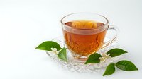 Glass cup of amber tea with fresh green leaves on crystal saucer against white background for beverage and wellness designs.