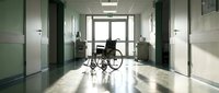 Empty wheelchair in modern hospital corridor with green walls and bright lighting creating shadows on polished floor for healthcare concepts.