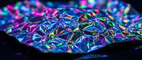 Holographic iridescent foil with rainbow prismatic reflections creating colorful geometric patterns on dark background for modern design projects.