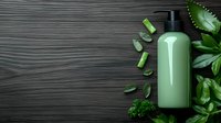 Green cosmetic bottle with fresh aloe vera pieces and tropical leaves on dark wooden background, natural skincare concept for beauty and wellness products.