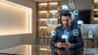 Man in business casual attire using smartphone with floating digital icons representing communication, data analytics and artificial intelligence technology in modern office environment.
