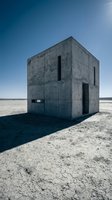 Minimalist concrete structure standing alone on barren salt flat landscape under clear blue sky, featuring brutalist architecture with geometric form and stark industrial design for conceptual projects.