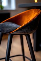 Modern bar stool with black velvet upholstery and copper-toned inner shell, illuminated by warm ambient light against blurred interior background.