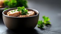 Homemade mushroom cream soup garnished with fresh parsley in dark ceramic bowl on black stone background, selective focus with copy space for menu design.