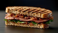 Grilled sandwich with crispy bacon, fresh lettuce, and tomato on toasted bread, captured in dramatic side view lighting against dark background. Perfect for menu design.