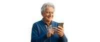 Senior man with gray hair and light skin tone, wearing a blue casual shirt, smiling while holding and looking at a smartphone. Isolated on white background for web and marketing use.
