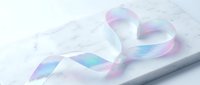 Iridescent holographic ribbon with rainbow reflections on white marble surface for luxury packaging and gift wrapping designs.