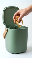 Hand dropping fruit and potato peels into a green compost bin with wooden handle, promoting sustainable kitchen waste recycling habits.