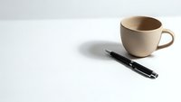 Minimalist workspace with beige ceramic coffee mug and black pen on clean white surface for office productivity and business planning concepts.