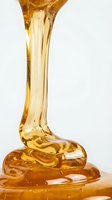 Golden honey dripping from wooden spoon onto surface, isolated on white background. Suitable for food, cooking, and culinary design projects.