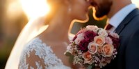 Romantic wedding moment with bride and groom in soft sunset light, featuring elegant bridal bouquet with pink and burgundy roses, baby's breath against blurred background.