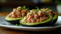Fresh avocado halves stuffed with diced salmon tartare and herbs on white plate. Healthy appetizer for restaurant menu and gourmet cooking concepts.