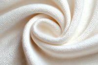 Soft white fabric swirled in elegant spiral pattern showing detailed textile texture and weave structure. Natural cotton or linen material with gentle folds and curves.