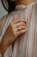 Close-up of Asian woman's hand with engagement ring against pleated white fabric, soft natural lighting creates romantic mood for wedding and jewelry photography.