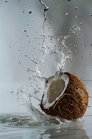 Fresh coconut half splashing into water creating dynamic splash pattern with droplets against light gray background for food and beverage advertising.