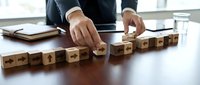 Businessman arranging wooden blocks with directional arrows on a conference table, symbolizing strategy, decision-making, and leadership in business.