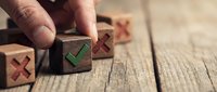 Hand placing wooden block with green check mark among blocks with red X marks on rustic table, symbolizing right choice and decision making.