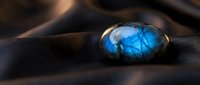 Stunning blue labradorite gemstone with iridescent flash resting on smooth dark stones in zen spa setting for meditation and healing practices.