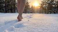 Barefoot person walking through pristine snow at golden sunset with evergreen forest creating peaceful winter wellness and mindfulness scene.