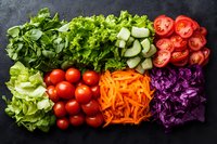 Fresh colorful vegetables neatly arranged in rows on dark stone background including lettuce, tomatoes, carrots, cabbage, cucumber and herbs for salad.