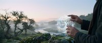 Person holding glowing digital brain hologram in hands against misty mountain landscape at dawn representing artificial intelligence and innovation.
