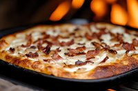 Homemade creamy carbonara pizza with crispy bacon bits and melted cheese baked in traditional stone oven, close-up view showing texture and toppings.