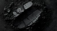 Crushed black eyeshadow or pressed powder makeup product on dark background showing texture and pigment details. Professional cosmetics photography.