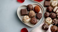 Assorted luxury chocolate truffles and pralines on heart shaped plate with red rose petals. Dark, milk and white chocolate bonbons with various toppings.