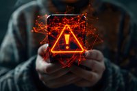 Glowing orange warning exclamation mark symbol in triangle hologram floating above hands holding smartphone, perfect for cybersecurity, digital threat and technology risk concepts.