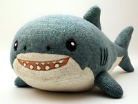 Cute plush shark toy with friendly smile and soft knitted texture in teal blue and cream colors against white background, isolated for design and marketing use.