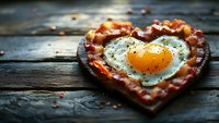 Heart shaped bacon frame with fried egg in center on rustic wooden background, romantic breakfast concept with crispy meat and sunny side up egg.