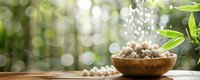 Fresh organic garlic cloves in rustic wooden bowl on table against blurred green garden background with bokeh lights and copy space for text.