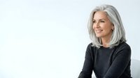 Mature woman with gray hair wearing dark sweater, smiling against white background. Suitable for healthcare, wellness, lifestyle, and senior-focused marketing materials.
