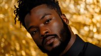 Young African American man with beard smiling confidently against golden bokeh background for professional headshot and business portrait photography.
