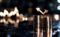 Stacks of silver coins with glowing upward arrows showing financial growth and investment success against blurred bokeh background in warm tones.