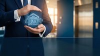 Businessman hands protecting house icon with smart home technology symbols in modern office environment for real estate and property insurance concepts.