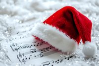 Red Santa hat resting on sheet music with musical notes surrounded by white artificial snow creating festive Christmas holiday atmosphere for seasonal celebrations.