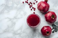 Fresh pomegranate juice in glass with whole fruits and seeds on marble background, vibrant red color contrasting with white surface.