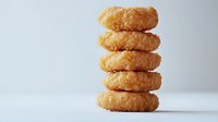 Stack of golden crispy onion rings piled vertically on white surface against light background, showcasing deep-fried breaded texture and layered composition.