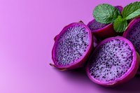 Fresh dragon fruit halves with vibrant pink flesh and black seeds on purple background with mint leaves, showcasing exotic tropical fruit in modern food photography.