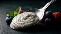 Creamy poppy seed pudding on spoon with fresh berries on dark surface, suitable for food photography, recipe blogs, and culinary content.